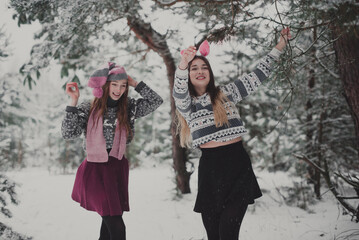 Close up fashion portrait of two sisters hugs and having fun winter time,wearing pink hats, rabbit ears and sweater,best friends couple outdoors, snowy weather