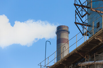 Obraz premium Pollution of the environment, ecology and air. Withdrawal of combustion products of soot, smoke and gases from the pipe of an industrial plant into the atmosphere against the background of a blue sky