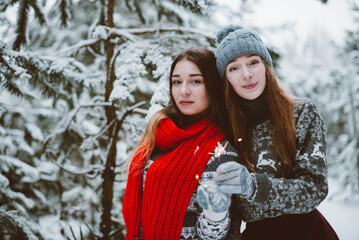 Fototapeta na wymiar Close up fashion portrait of two sisters hugs and having fun, holding sparklers in winter time forest, wearing sweaters and scarfs,best friends couple outdoors, snowy weather