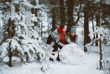 Fototapeta na wymiar Close up fashion portrait of two sisters hugs and having fun, make snowman in winter time forest, wearing sweaters and scarfs,best friends couple outdoors, snowy weather