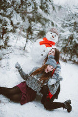 Fototapeta na wymiar Close up fashion portrait of two sisters hugs and having fun, make snowman in winter time forest, wearing sweaters and scarfs,best friends couple outdoors, snowy weather