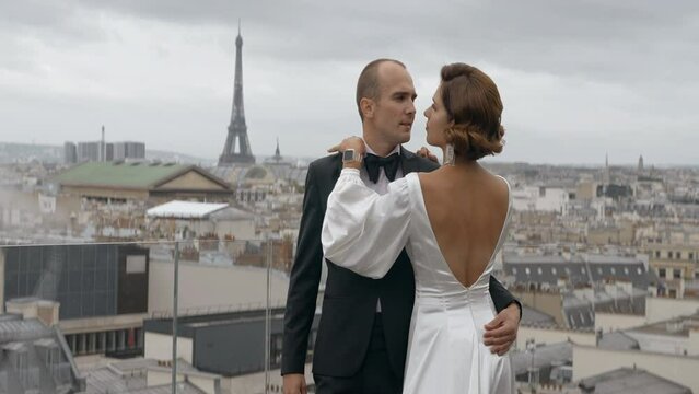 Couple enjoying each other on the background of Paris cityscape. Action. Elegant man in suit and woman in dress embracing in front of the Effel tower.