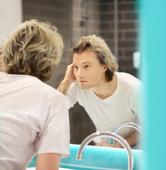 Obraz premium young man looking in the mirror,combing his hair,looking at problems on face.