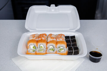Box of Philadelphia rolls. Fast delivery sushi in a white container. Jar of soy sauce for sushi