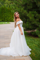 a blonde bride on a path in the park in a white long dress.