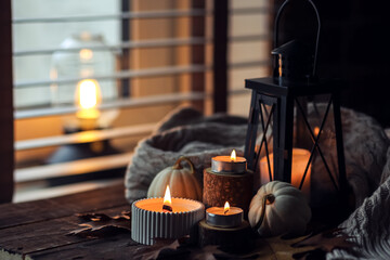 Cozy autumn composition with aromatic candle, pumpkins, wool sweater, leaves, cinnamon. Aromatherapy on a grey fall morning, home atmosphere of cosiness and relax. Wooden background close up.