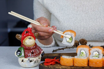 Japanese Philadelphia rolls on a wooden cutting board on a table in the kitchen. The girl is holding food with chopsticks. Christmas decoration. New Year concept