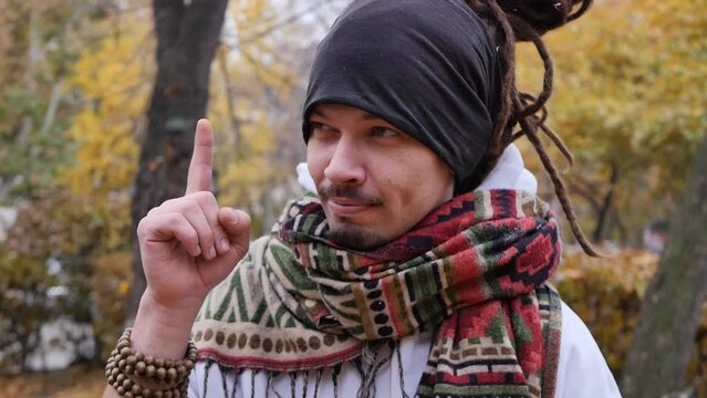 A young handsome man with dreadlocks and a stylish beard and mustache shows a gesture with his index finger up, meaning a new thought or idea. Handsome mixed race man with scarf around his neck