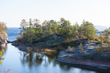 Ladoga skerries on the lake. A beautiful view of the rocky shores covered with pine trees. Nordic nature at sunset. Stunning view of islands and archipelago. National Park of Karelia