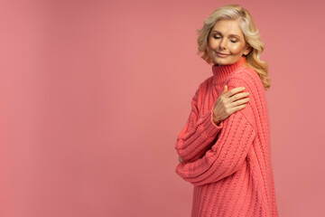 Beautiful happy mature woman wearing stylish winter sweater isolated on pink background, copy space. Shopping concept 