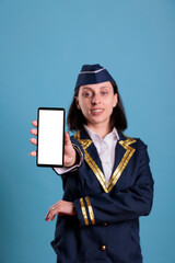 Smiling flight attendant showing modern phone with blank white screen, smartphone app advertising mockup. Plane air hostess holding telephone with empty display for web promotion
