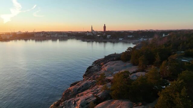 Aerial view over the rocky coast towards the skyline of Hanko city, spring sunset in Finland