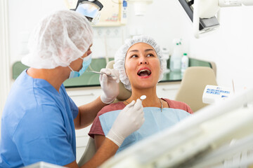 Qualified man dentist in a protective mask conducts an examines of a woman patient sitting in a dental chair in the clinic