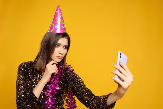 pretty young woman wearing pink party hat and boa around her neck looking at her smartphone with sad face
