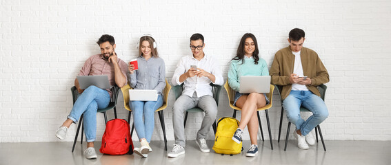 Students with modern devices sitting near light wall
