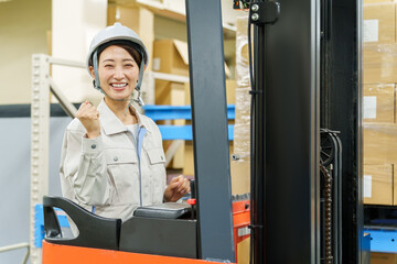 フォークリフトに乗ってガッツポーズをする女性作業員
