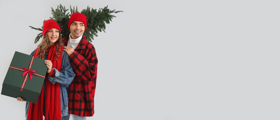 Young couple in love with Christmas tree and gift on grey background with space for text