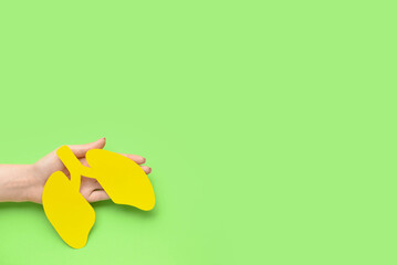 Female hand and yellow paper lungs on green background