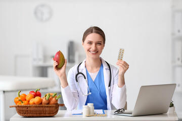 Female doctor with vitamins and mango sitting at table in clinic