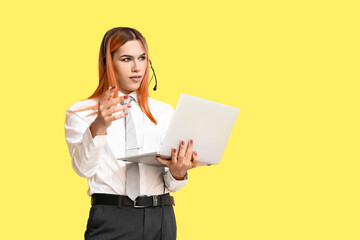 Beautiful transgender secretary in headset with laptop on yellow background