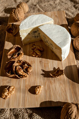 Composition of a cut cheese head with white and green mold and walnuts on a bamboo board on a background of burlap