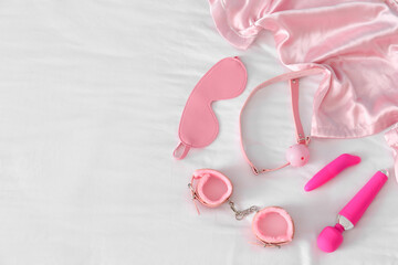 Pink sex toys with pajamas on white bed, top view