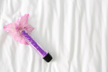 Purple vibrator with flower on white bed, top view