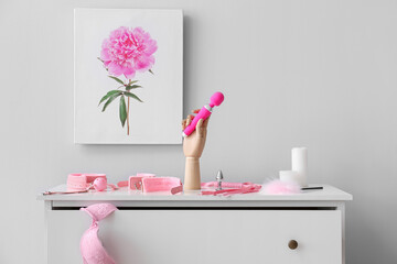 Wooden hand with pink sex toys on chest of drawers near light wall