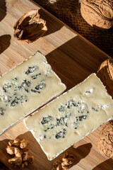 Composition of a cut cheese head with white and green mold and walnuts on a bamboo board on a background of burlap