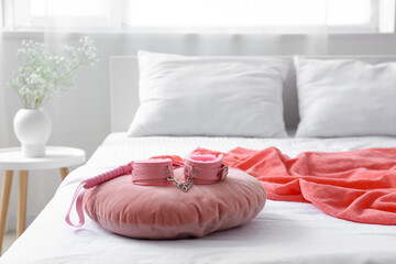 Pillow with pink vibrator, feather stick and handcuffs on bed in room