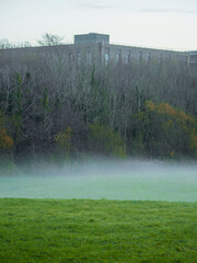 Scene in a park with fog over the grass. Dark and moody atmosphere. Nobody. Nature landscape. Construction site in the background.