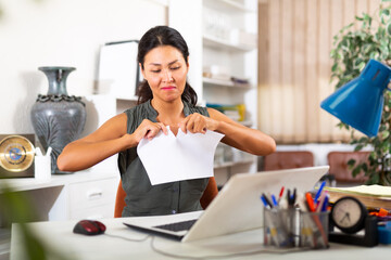 Furious asian businesswoman tearing up paper in office at workplace