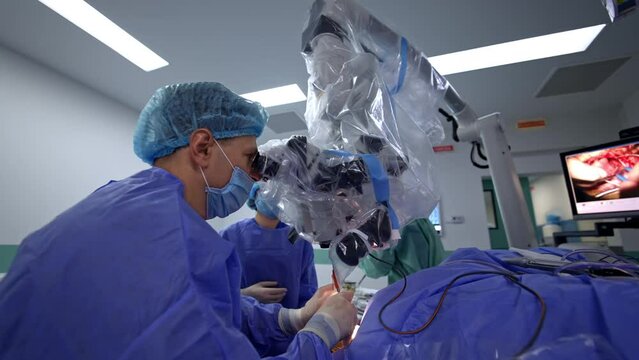 Doctor carefully applying the instruments in the patient&rsquo;s cut and the process is shown at the screen. Neurosurgeon looks intently in the microscope at surgery.