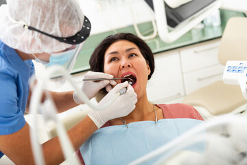 Man dentist holding dental drill and treating teeth of asian woman in dentist office