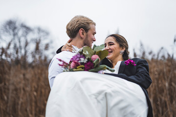 Wedding day. Groom holding his bride in a white dress in his arms. Outdoor photoshoot. High quality photo