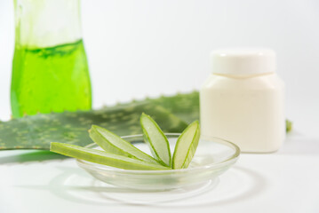pieces of Aloe Vera leaf, glass container, plastic and detergent bottle on a table