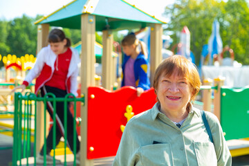 Positive grandma watches her grandchildren walking on a playground on a sunny day in Russia