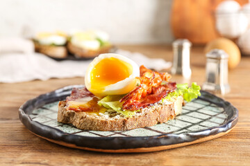 Plate of delicious toast with boiled egg and fried bacon on wooden table, closeup