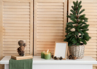 Christmas tree, frame, candles and fir cones on mantelpiece near folding screen