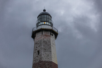 Montauk Point  Lighthouse at Montauk State Park in East Hampton, Long Island, New York. The tower is under construction awaiting new paint. Storm clouds above - obrazy, fototapety, plakaty