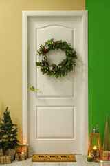 White door with Christmas wreath, fir trees and presents in hall