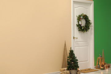 Fototapeta na wymiar White door with Christmas wreath, fir trees and presents in hall