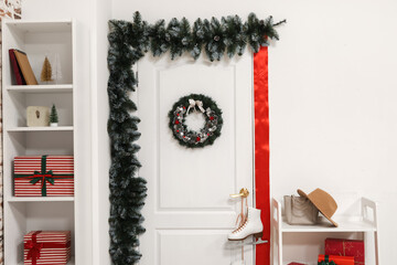 White door with Christmas wreath, fir branches and skates in hall