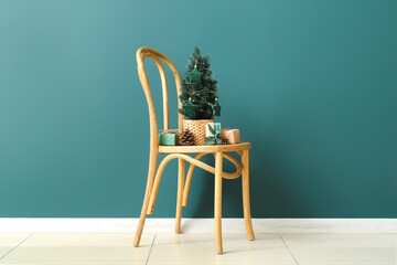 Small Christmas tree with pine cones and gifts on chair near green wall