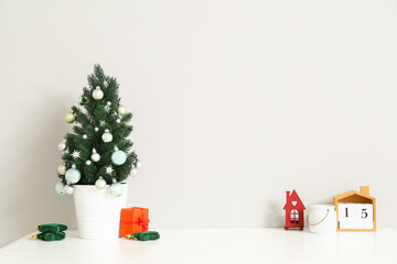Small Christmas tree with toys on table near light wall