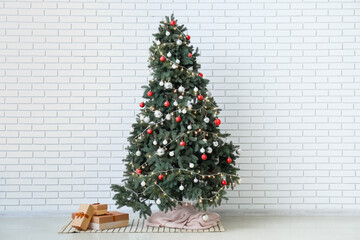 Glowing Christmas tree with presents near white brick wall