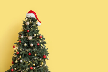 Glowing Christmas tree with Santa hat near yellow wall