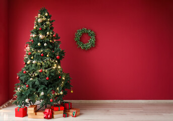 Glowing Christmas tree with presents and wreath on red wall
