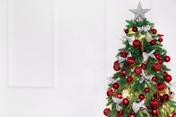 Glowing Christmas tree with decor near light wall
