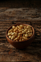 Old and rusty wooden table with a wooden bowl with shelled peanuts and some peanuts and in the wooden ladle, selective focus